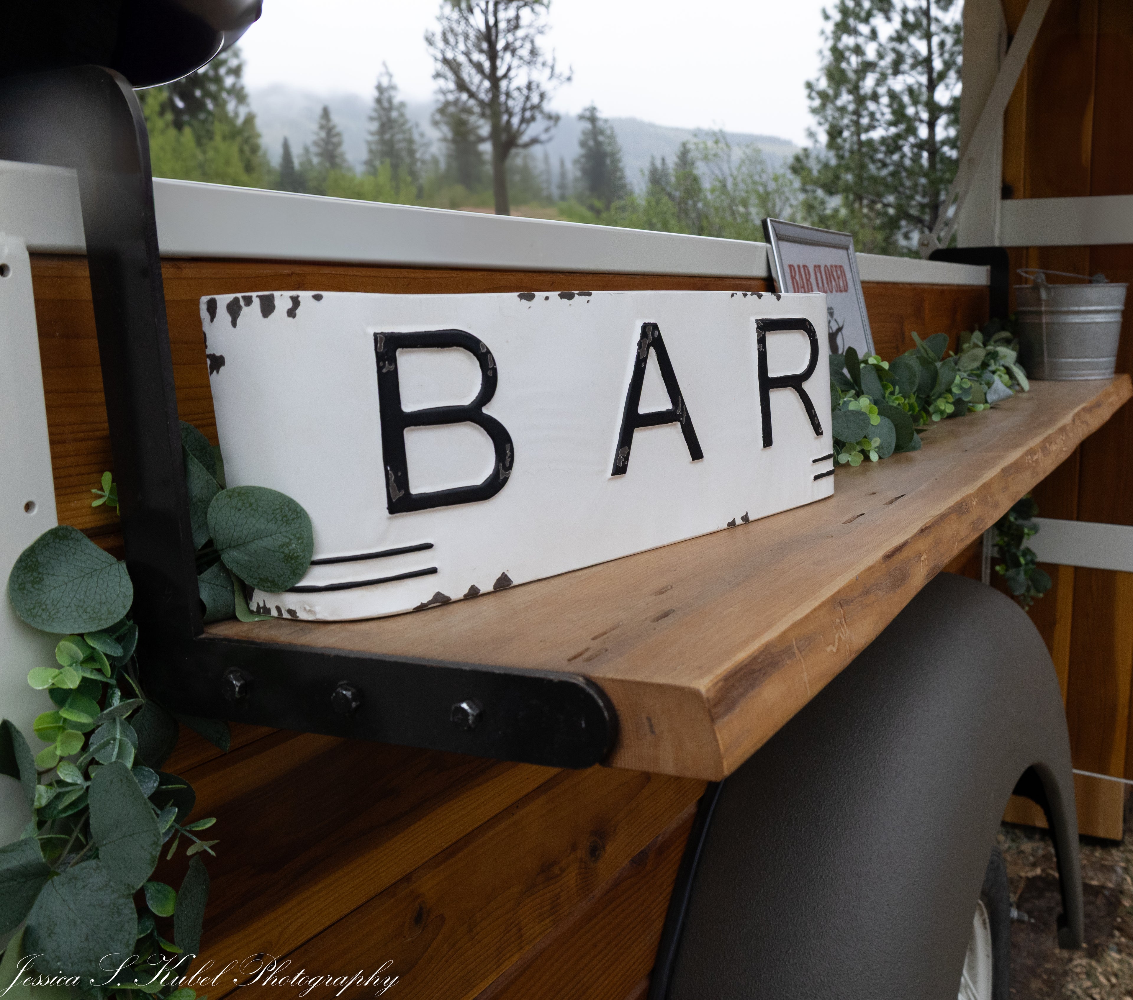 Metal sign with 'BAR' on a rustic truck bed outdoors